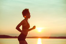 Attractive Young African Girl Athlete Running At Sunset Along The Beach. Fitness Training Of Runner.
