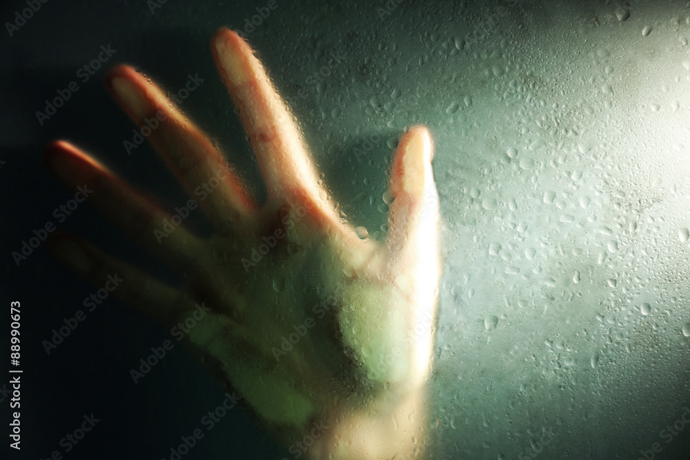 Female hand behind  wet glass, close-up