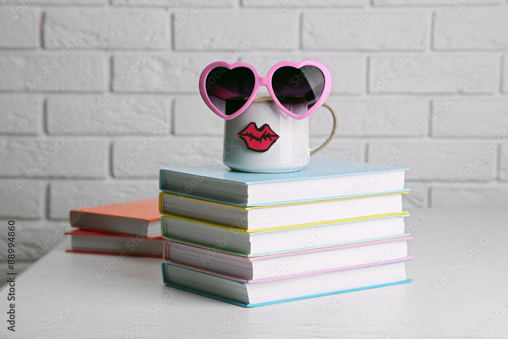 Books and cup with lips on wooden table on brick wall background