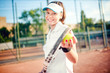 © aboutmomentsimages - Portrait of woman playing tennis, holding racket and ball. Attractive brunette girl wearing white t-shirt and cap on tennis court