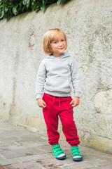 Wall Mural - Fashion portrait of adorable toddler boy wearing grey sweatshirt, red trainings and green shoes