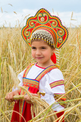 girl in Russian national a dress with ears in hands  stand in the field of the ripening wheat