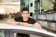 Young man sitting on his car's door, resting on the roof