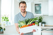canvas print picture - Junger Mann mit Gemüsekiste in der Küche