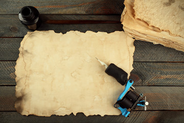 Wall Mural - Machine for tattoo with old paper and bottle of ink on table close up