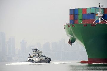 Tugboat approaching Shipping Container fully loaded with cargo coming into port