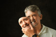 © Michael O'Keene - An angry, emotional, depressed, bipolar disorder man is revealing his true self as he takes off a fake smile happiness mask that looks exactly like his face.