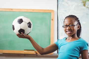 Wall Mural - Smiling pupil holding football in a classroom 