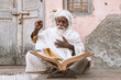 Close up of an old indian sadhu (saint) sitting and reading sacred texts near the temple. 