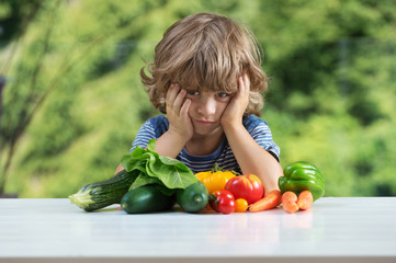 Cute little boy sitting at the table, unhappy with his vegetable meal, bad eating habits, nutrition and healthy eating concept