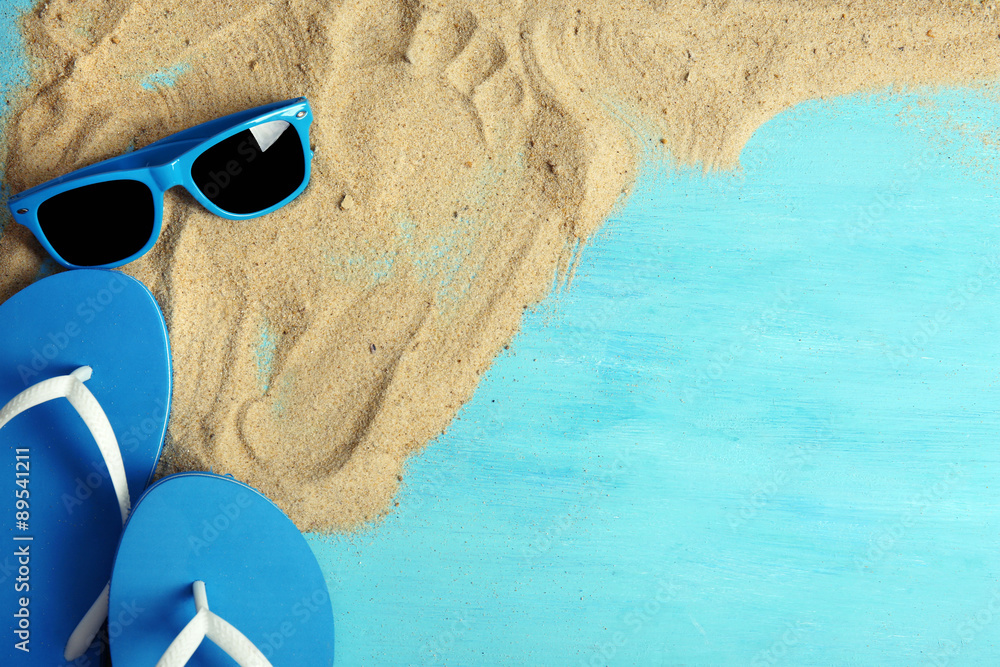 Flip flops and sunglasses with sand on wooden background