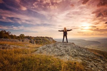 Wall Mural - a woman on the top of a rock enjoys the view of sunset over an autumn forest