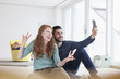 © Westend61 - Smiling young couple taking a selfie with smartphone in the living room