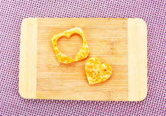 Poster - Cheese slice with cut in shape of heart on wooden background