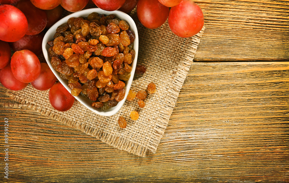 Raisins in bowl with grapes on table close up