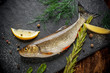 Fresh fish ide on a black stone slab surrounded by herbs, slices of lemon