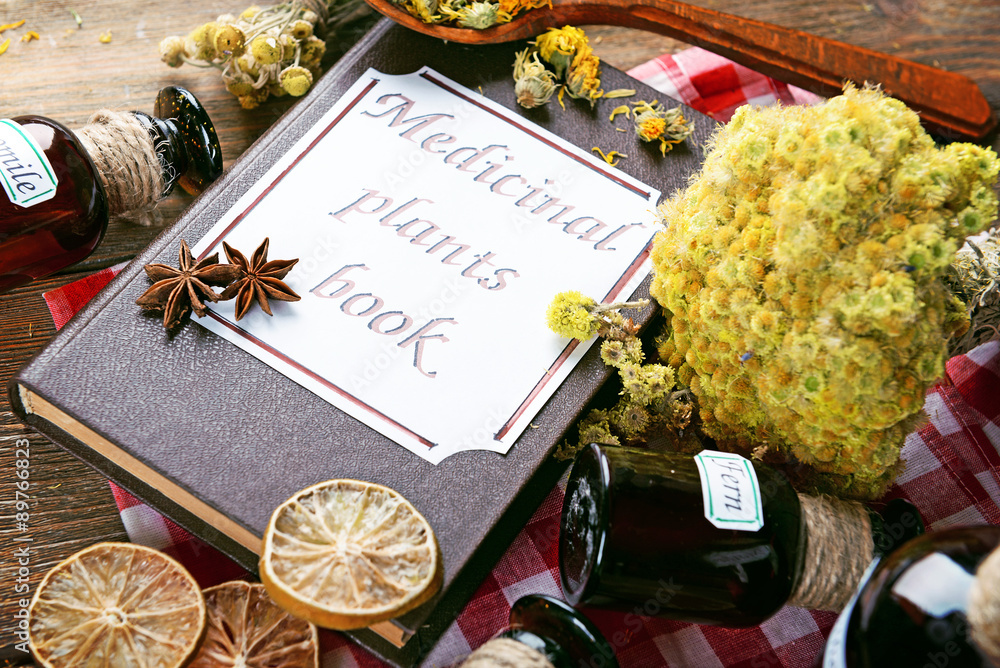 Medicinal plants book with dried herbs and bottles on table close up