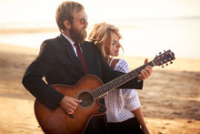 Guitarist And Blonde Girl Standing On Sandy Beach