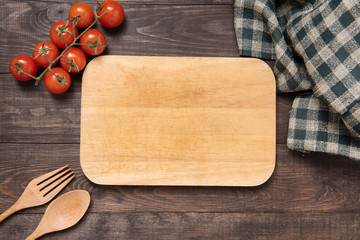 Wall Mural - Cutting board with tomato, fork and spoon on wooden background