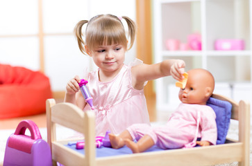 little girl playing doctor with her newborn baby doll in room