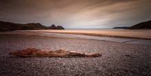 Driftwood And Pebbles At Three Cliffs Bay On The Gower Peninsular, South Wales.