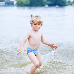 Wall Mural - Little blond kid boy having fun with splashing in a lake, outdoo