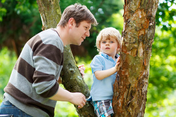 Cute little kid boy enjoying climbing on tree with father, outdo