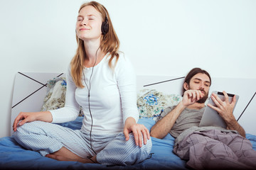 young caucasian couple in bed using tablet and listening music