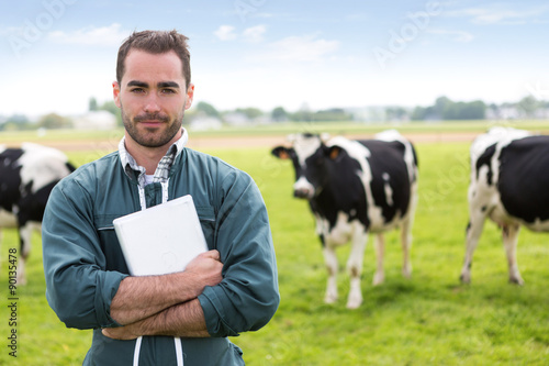 Fotografía Portrait of a young attractive farmer in a pasture with cows