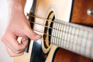 Young man playing on acoustic guitar close up