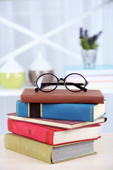 Canvas Print - Stack of books with glasses on wooden table in room