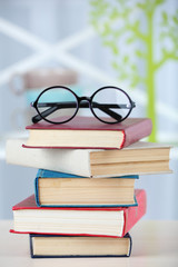 Canvas Print - Stack of books with glasses on wooden table in room