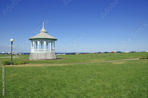 Fotografie, Obraz White Gazebo on green grass lawn with blue skies in Cape Cod, New England, USA
