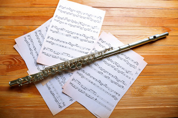 Wall Mural - Silver flute with music notes on wooden table close up