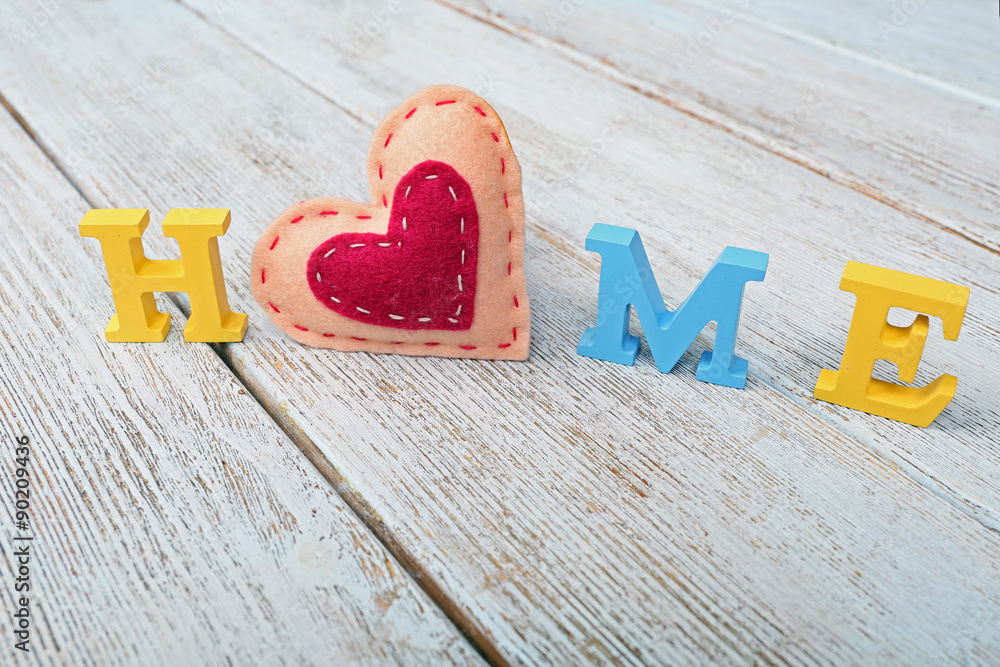 Decorative letters forming word HOME with heart on wooden background