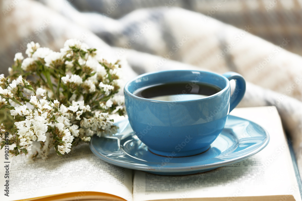 Blue cup of coffee with open book on sofa in room