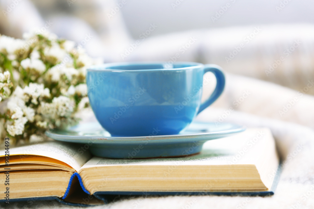 Blue cup of coffee with open book on sofa in room