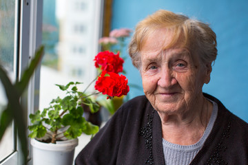 Portrait of elderly woman standing on the balcony among the flowers.