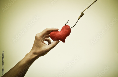 Fotografia, Obraz hand trying to catch a red heart on a fish hook - Love trap concept