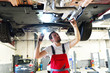 Mechaniker in einer Werkstatt kontrolliert den Unterboden eines Autos // mechanic in garage checked car