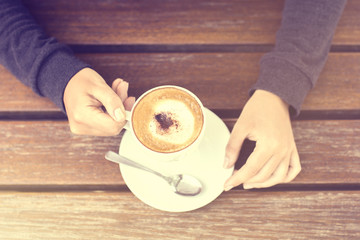 Wall Mural - Girl holding a cup of cappuccino and wooden table