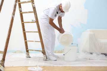 Wall Mural - painter man at work pour into the bucket color for painting wall