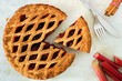 Strawberry and rhubarb pie with cut piece on a marble background, overhead scene