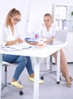 © lenets_tan - Two women working together at office, sitting on the desk