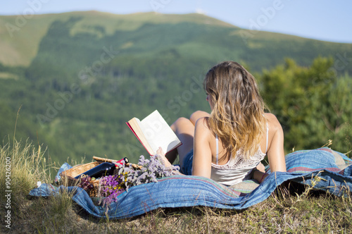 Fotografie, Obraz Girl laying on a blanket and reading a book on a picnic in the f