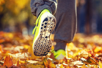 Wall Mural - Runner woman feet running on autumn road closeup on shoe. Female fitness model outdoors fall jog workout on a road covered with fallen leaves. Sports healthy lifestyle concept.