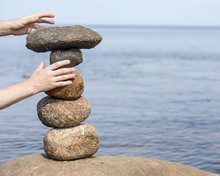 Human Hand Making Stack Of Large Round Stones Near The Water, Which Are Due To The Balance