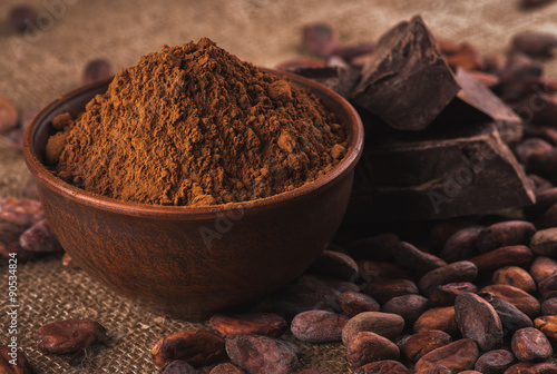 Fotografía cocoa powder in a brown ceramic bowl, raw cocoa beans in the pee
