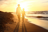 Fototapeta Fototapety z morzem do Twojej sypialni - Spacer po plaży, zachód słońca. Dzieci chłopiec i dziewczynka spacerują brzegiem morza