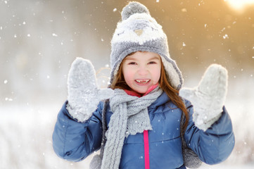 Wall Mural - Funny little girl having fun in beautiful winter park during snowfall